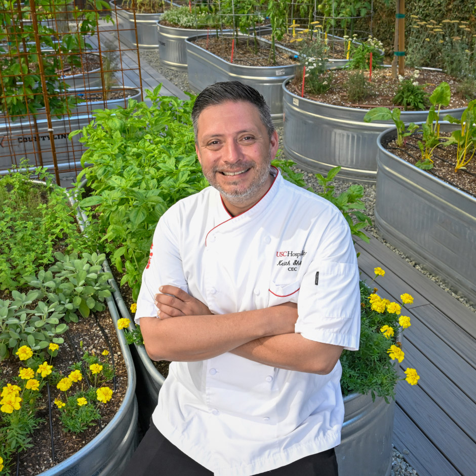 USC Hospitality chef posing in front of raised herb beds in the campus Teaching Garden